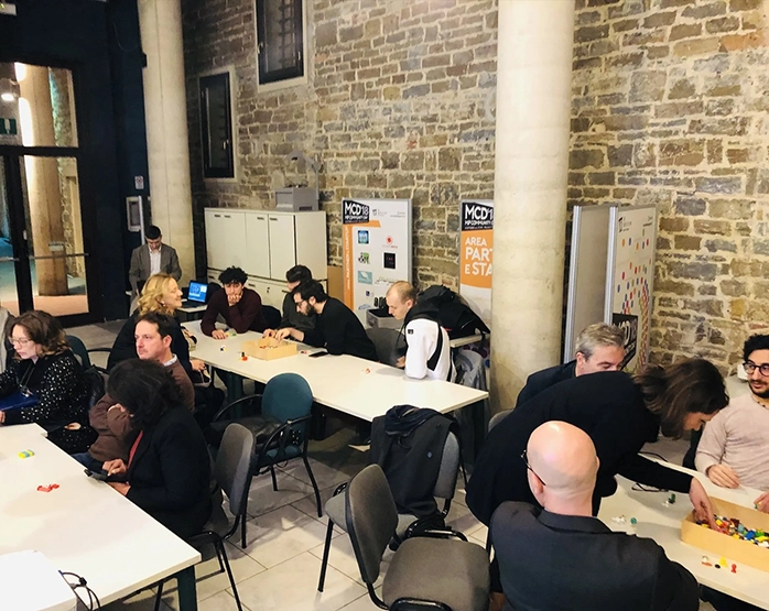 Partecipanti seduti a tavoli durante un workshop collaborativo alla Sala Hack di Firenze, in occasione dell’evento 'Digital Humanities: relazioni umane cyborg?' del 28 febbraio 2019.