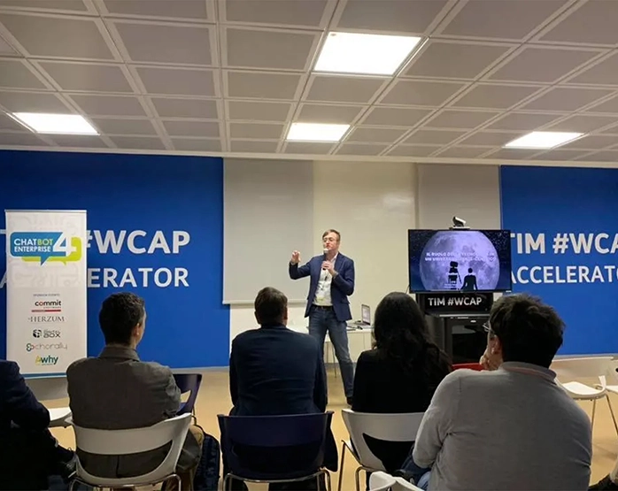 Giacomo Bosio sul palco durante l’evento 'Il ruolo della tecnologia in un universo cliente-centrico', con pubblico in sala e banner TIM WCAP sullo sfondo.
